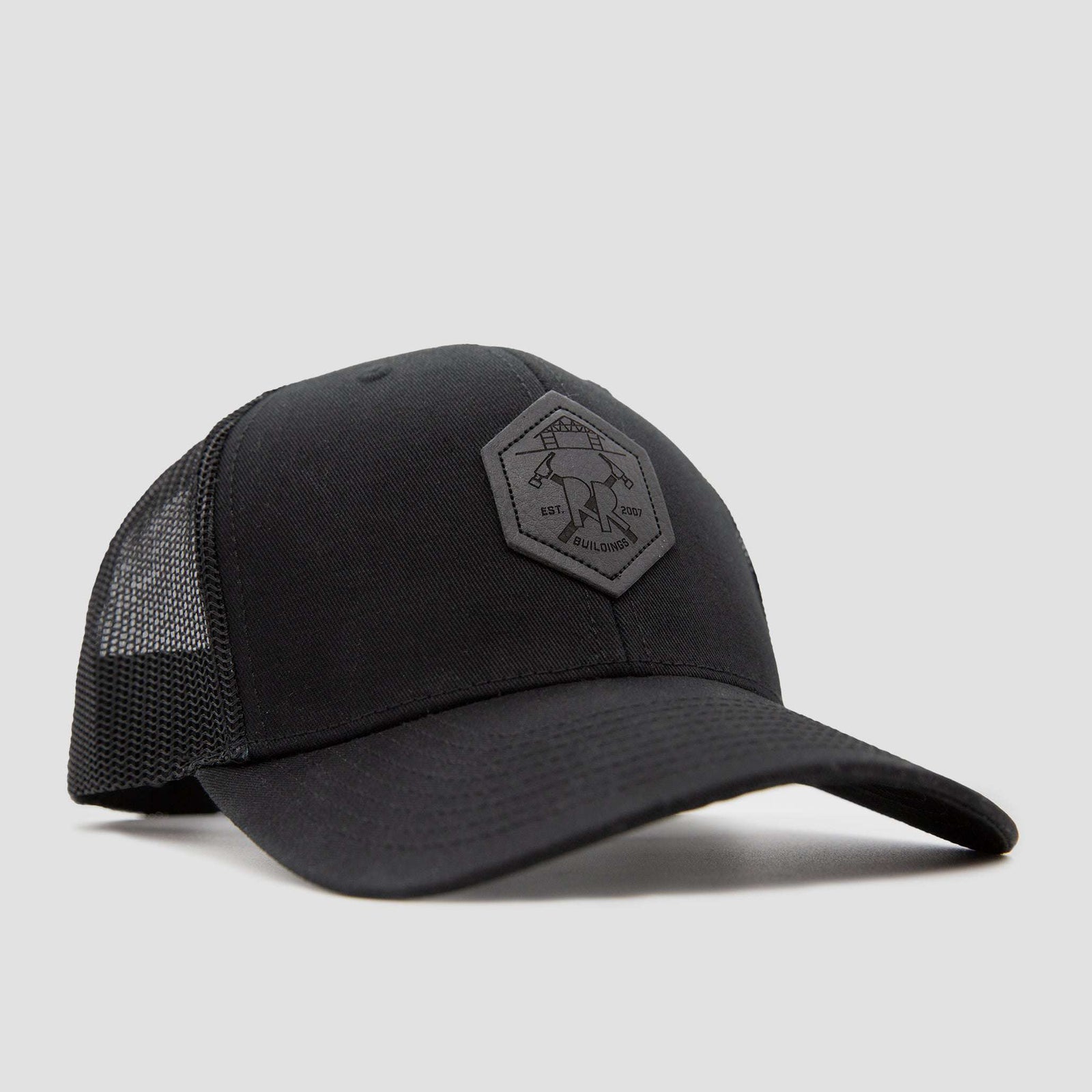 Front view of a black baseball cap with a hexagonal patch on the front, featuring a logo with two crossed hammers and text that reads EST 2007 and BUILDINGS on a plain light gray background.