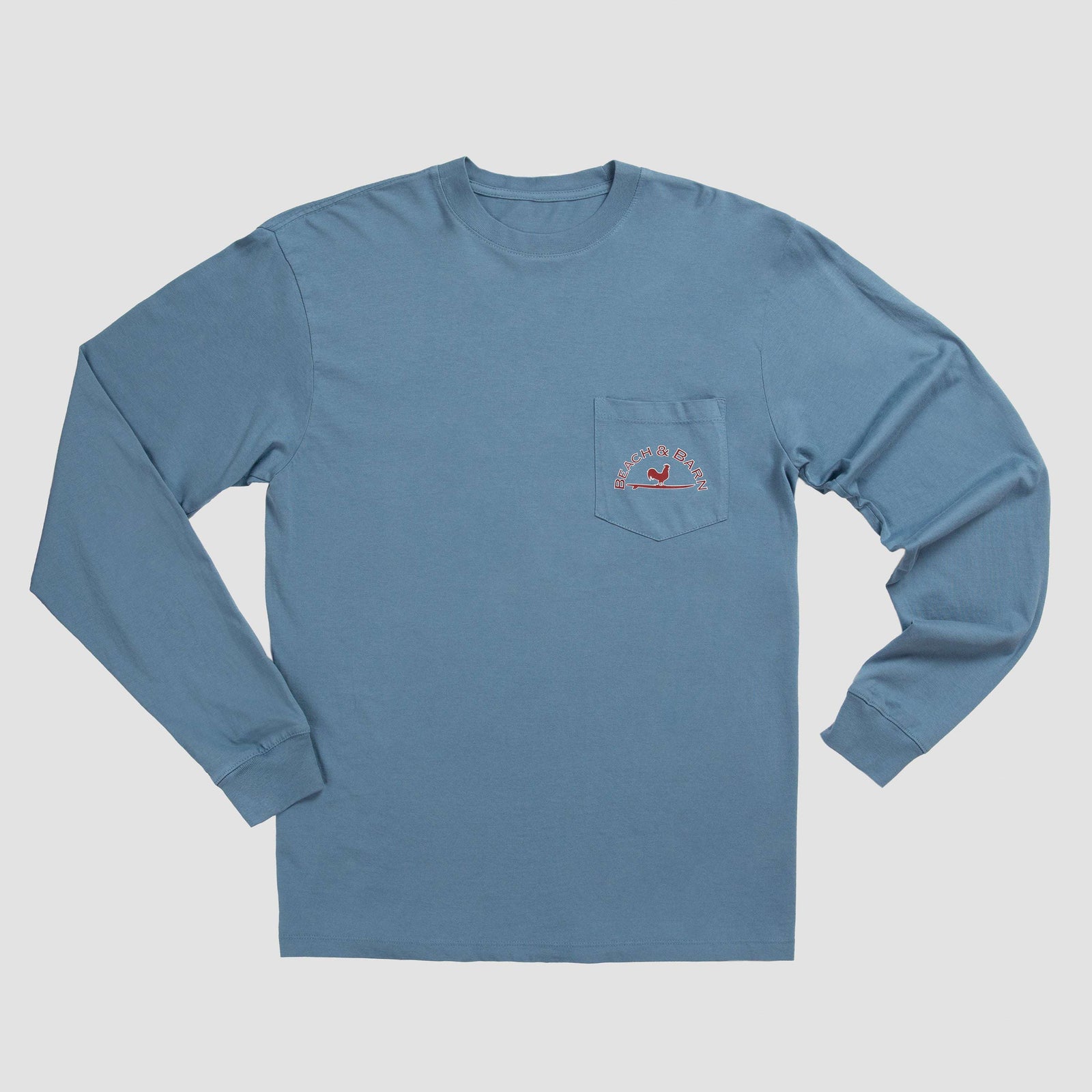A blue long-sleeve shirt with a large red and white circular Beach & Barn logo on the back, featuring a rooster silhouette and the words Wilmington, NC, Est. 2016.